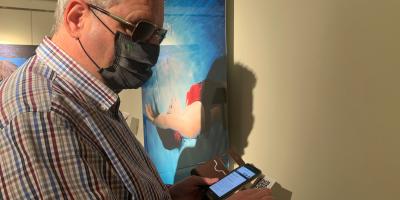 Una persona ciega utiliza su móvil para escuchar la música asignada por Inteligencia Artificial a la fotografía expuesta. | Foto: ONCE